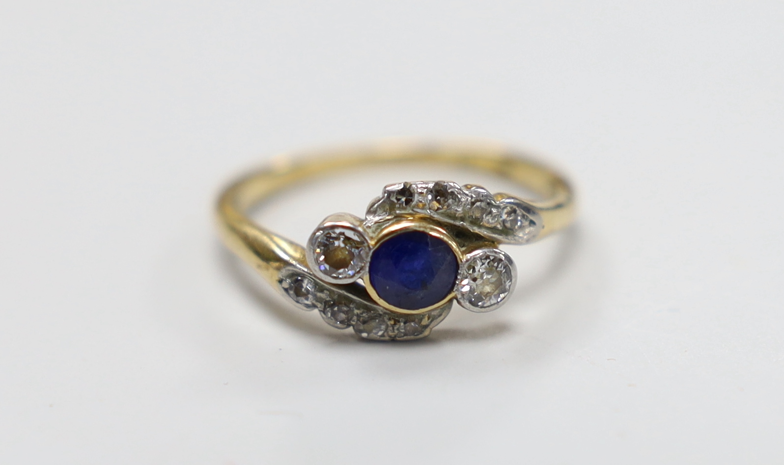 An 18ct, single stone sapphire and two stone diamond crossover ring, with diamond set shoulders, size L, gross weight 2.9 grams.